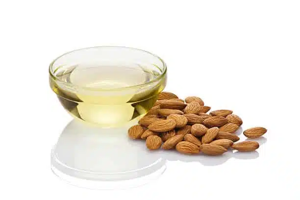 Glass bowl filled with almond oil and some almond nuts isolated on white background