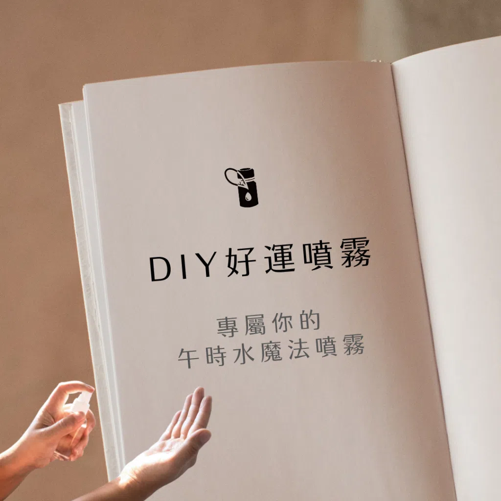 畫面以奶色系精裝書籍空白頁為背景，頁面中央黑色精油瓶圖示下方文字「DIY好運噴霧／專屬你的午時水魔法噴霧」，左下角有雙手正在噴灑精油噴霧，背景柔和窗光斜射在淺米色亞麻布上，整體營造出手作精油噴霧帶來好運與魔法感的氛圍。