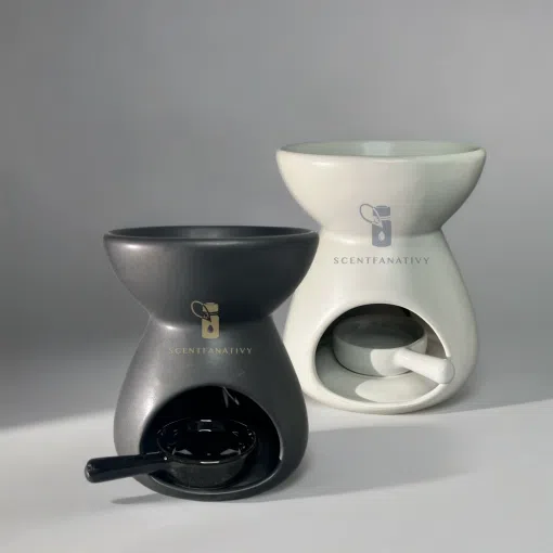 這張圖片展示了兩款 SCENTFANATIVY 品牌的陶瓷精油燈──一款霧面黑色與一款純淨白色。產品採用現代極簡風設計，碗狀上部用於放置香薰蠟或精油，下方圓弧開口可放置茶燭作為加熱來源。高質感陶瓷材質與柔和光影相映，完美呈現產品的工藝細節與質感。這款黑白雙色的「陶瓷精油燈」非常適合用於家居香氛、辦公室擴香、瑜伽室放鬆或送禮，兼具實用與美感。關鍵詞包括：陶瓷精油燈、香薰擴香、家用香氛、極簡設計、黑色精油爐、白色精油爐、SCENTFANATIVY